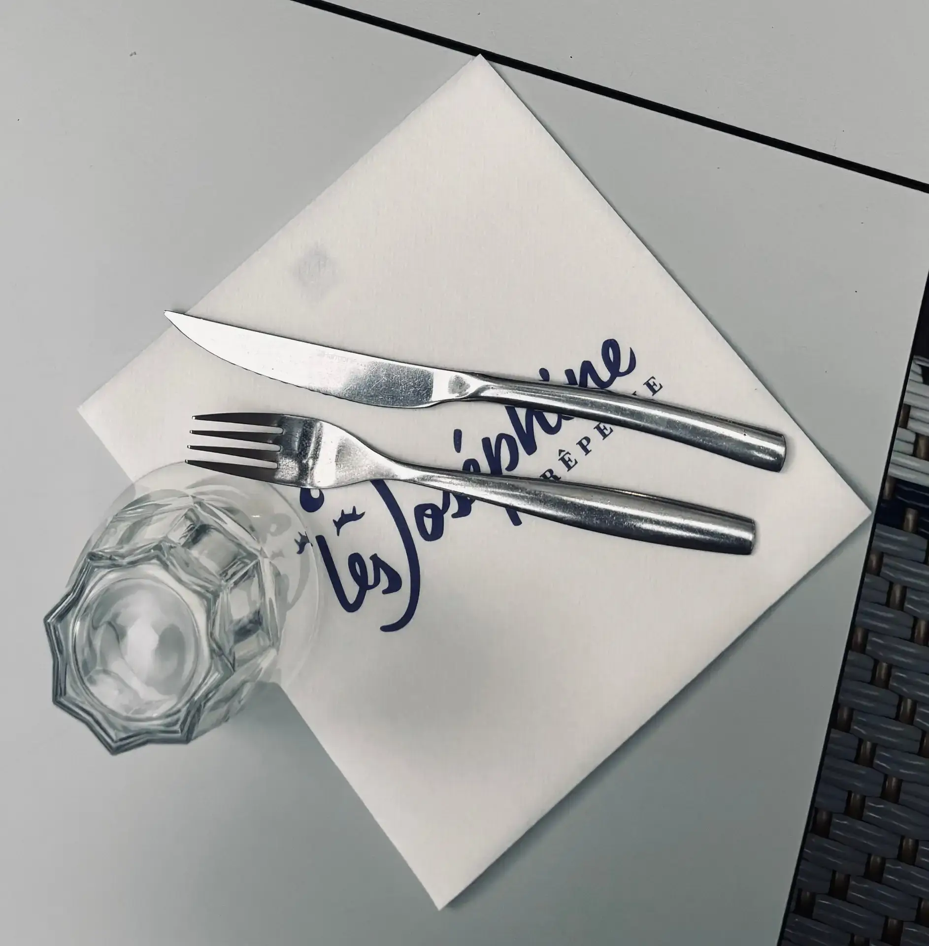 Dressage de table soigné avec couverts inox, verre à eau et serviette logotée Crêperie Les Joséphine à Vannes.